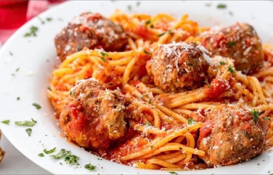 Spaghetti and meatballs in tomato sauce on a white plate, garnished with herbs