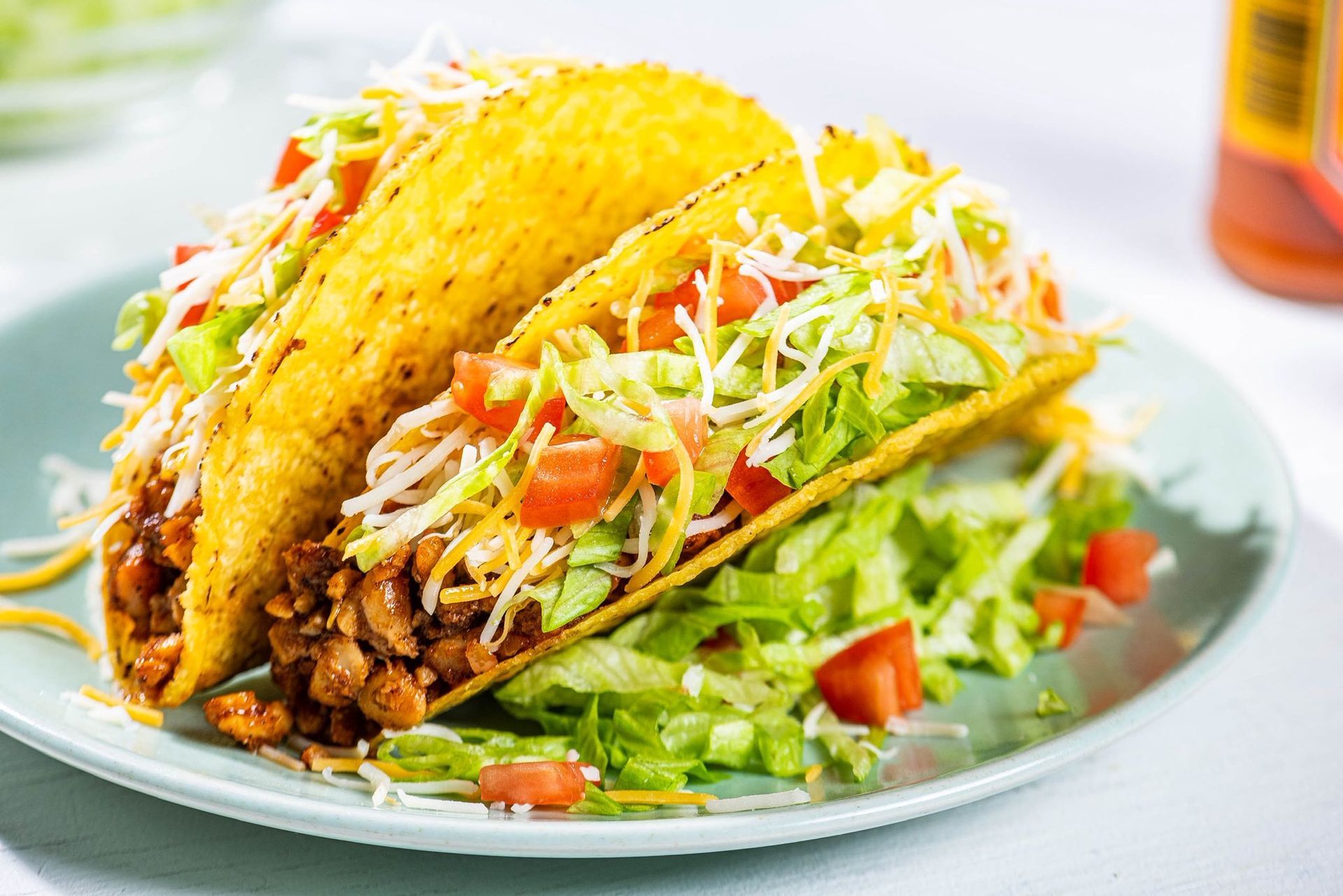 Two tacos on a plate with lettuce, tomatoes, and shredded cheese
