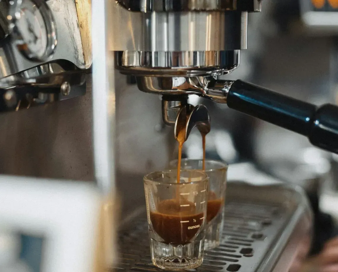 Espresso machine pouring coffee into a small glass cup on a metal drip tray.