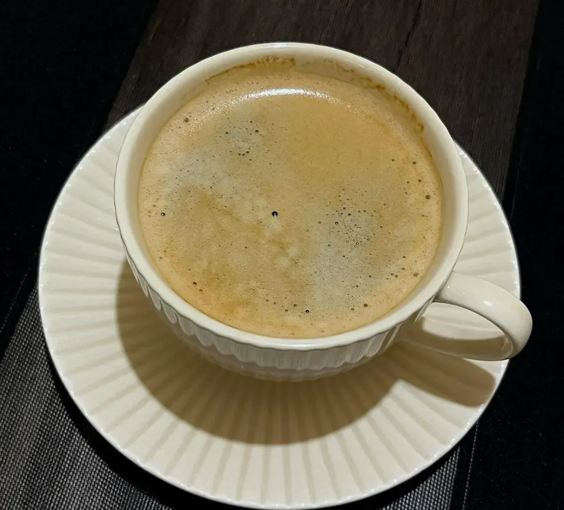 White coffee cup of espresso on a saucer atop a textured dark tablecloth