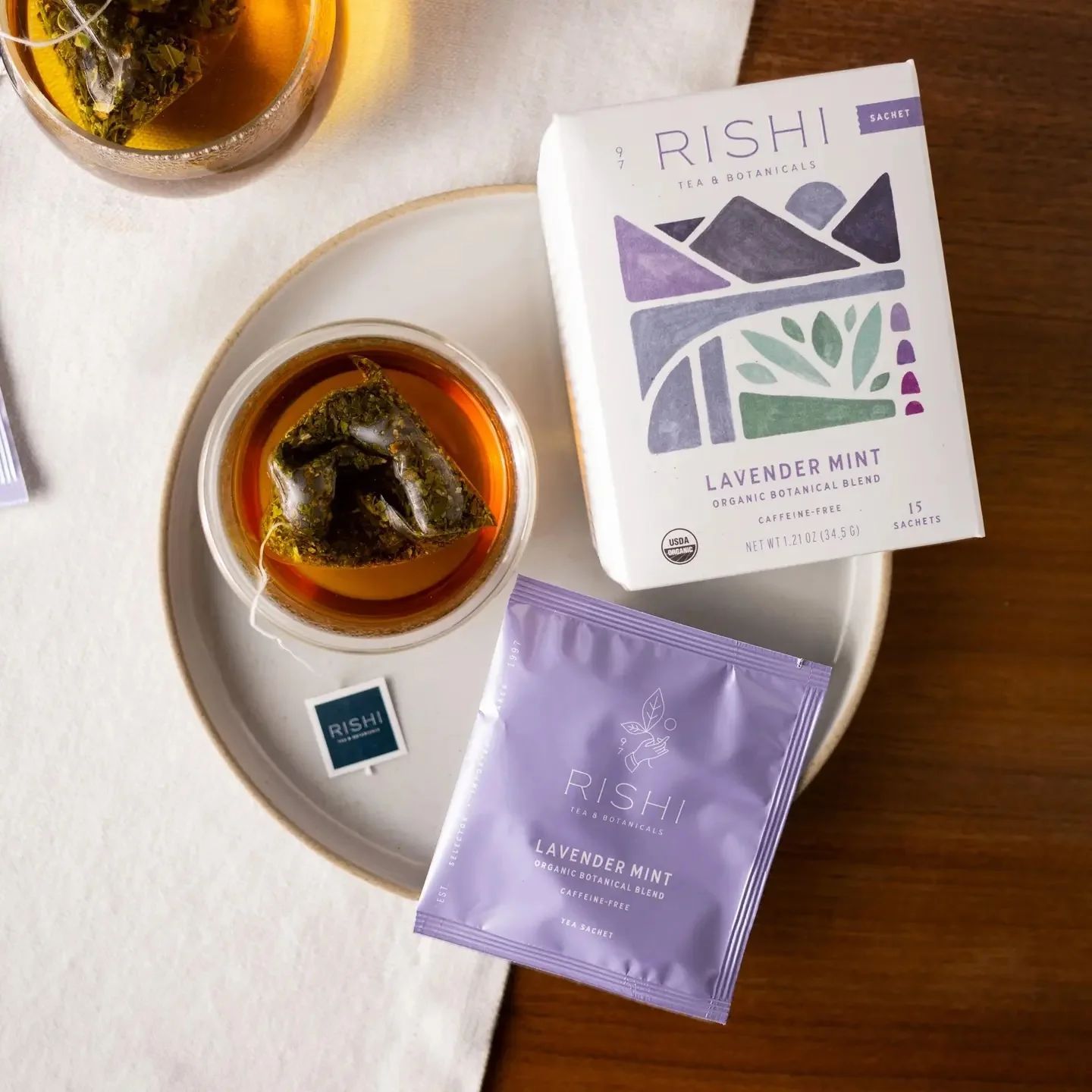 Lavender mint tea box and sachet beside two glass cups on a white table