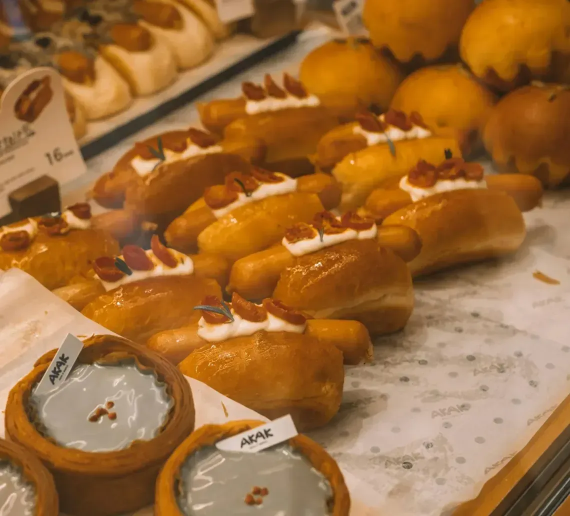Bakery display of assorted pastries and breads on a marble counter, with price tags and tarts in front