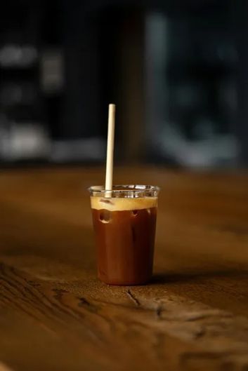 Iced coffee in a clear plastic cup with a straw on a wooden table.