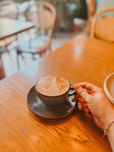 Hand holding a latte in a black cup on a wooden café table