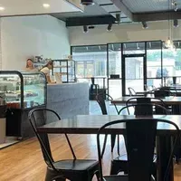 Café interior with black chairs, wooden tables, display case, and two staff behind the counter