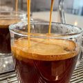 Espresso being poured into a clear glass cup, with crema forming on top