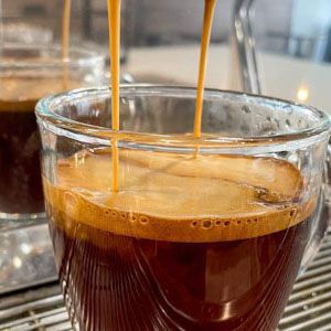 Espresso being poured into a clear glass cup, with crema forming on top