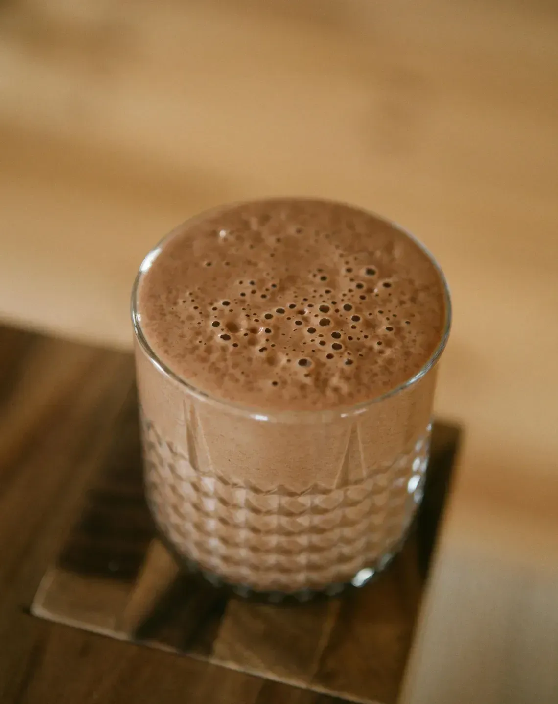 A glass of chocolate milk or cocoa on a wooden tray, seen from above.