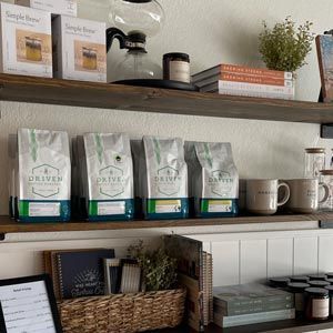 Wooden shelves with coffee bags, mugs, jars, and a wicker basket in a cozy shop display