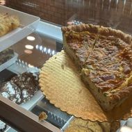 Bakery display with a large slice of quiche on a metal tray and pastries in the case