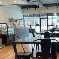 Café interior with black chairs, wooden tables, display case, and two staff behind the counter