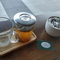 Glass tea pot, empty cup, and small white bowl on a wooden table with a green card.