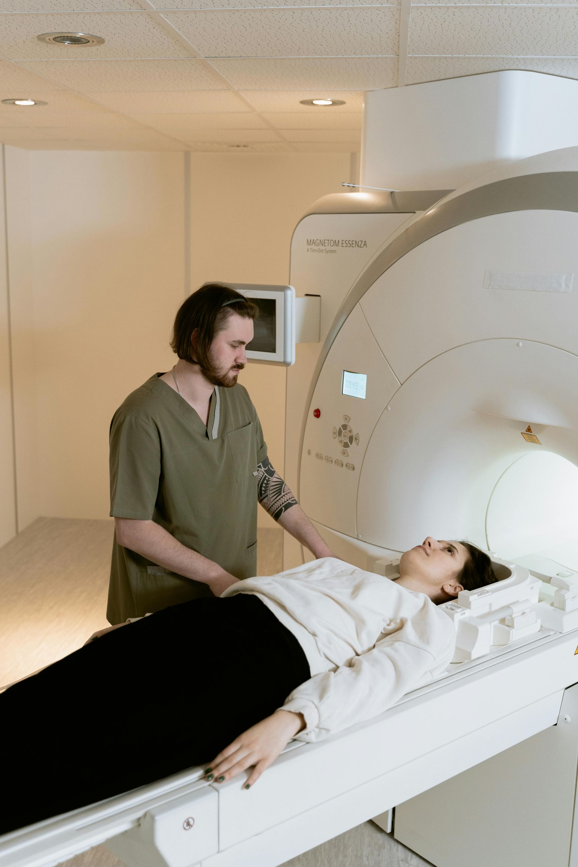 A man is standing next to a woman laying on a mri machine.