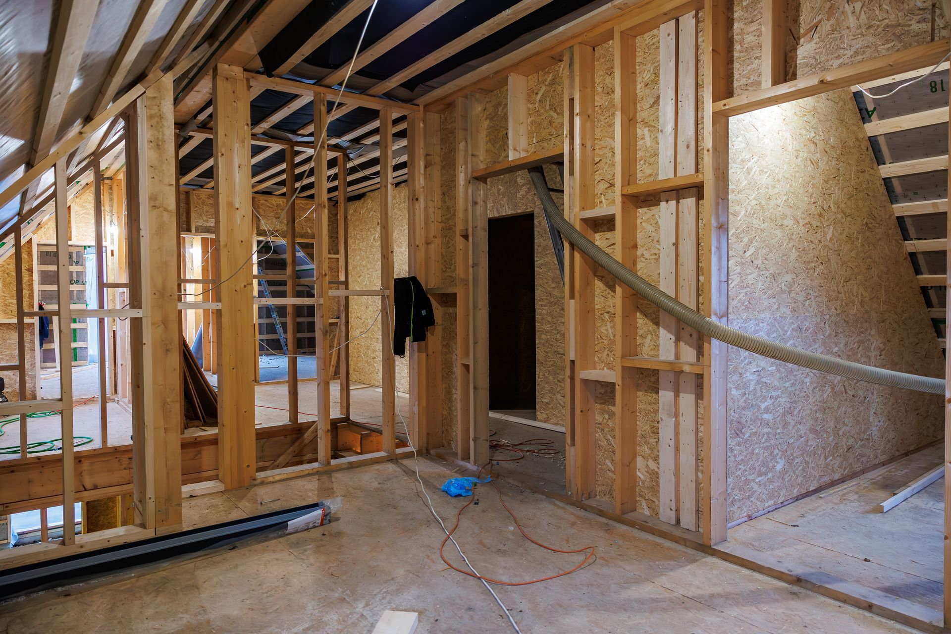 The interior of an unfinished home showing wooden wall framing, oriented strand board paneling, and an open stairwell. The interior of an unfinished home showing wooden wall framing, oriented strand board paneling, and an open stairwell.