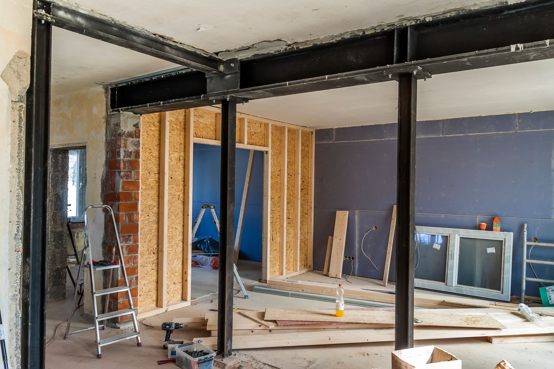 Interior construction site showing structural steel beams supporting a ceiling and partially framed wooden walls. Interior construction site showing structural steel beams supporting a ceiling and partially framed wooden walls.