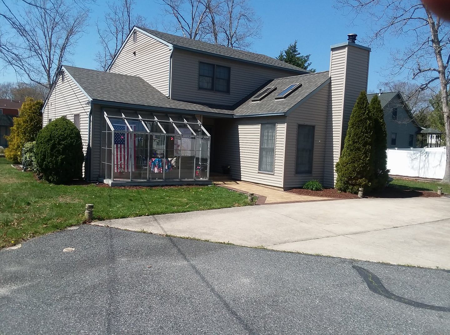Two-story house with sunroom, chimney, and driveway on a sunny day.