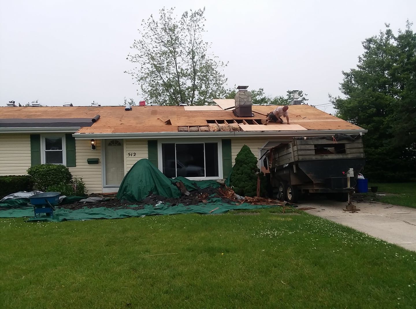 House with partially removed roof, debris in yard, and a person working.