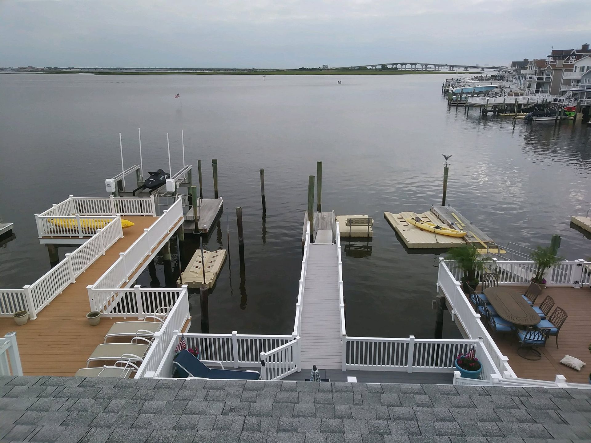 Docks with boats on a calm body of water, several homes in the background under an overcast sky.