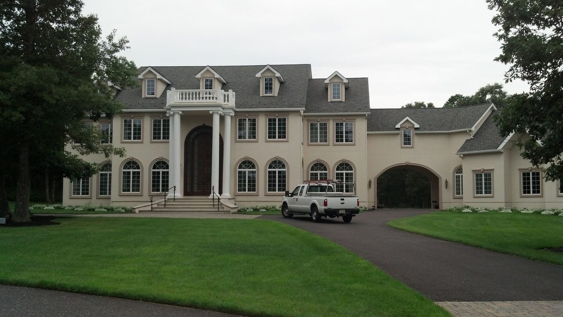 Large, light-colored house with columns and many windows, a pickup truck parked in front, and a green lawn.