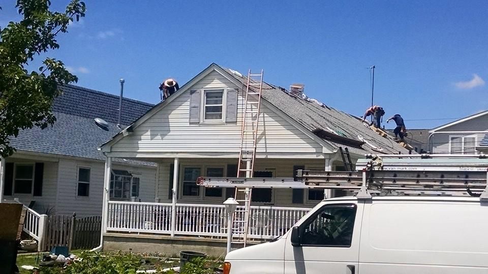 Roofers working on a house roof on a sunny day. White van parked nearby.