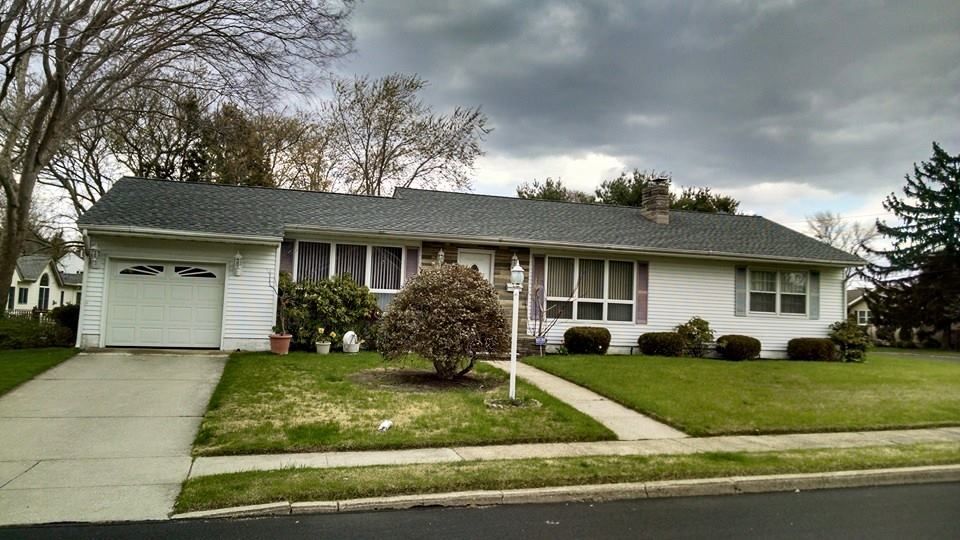White ranch-style house with attached garage, green lawn, sidewalk, and cloudy sky.