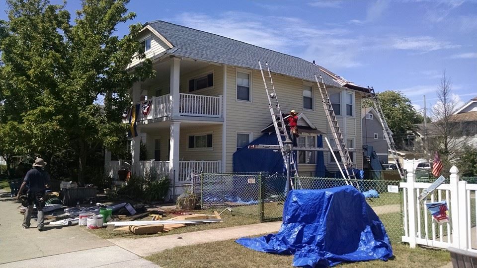 House under construction, roof being worked on, ladders and tarps visible.