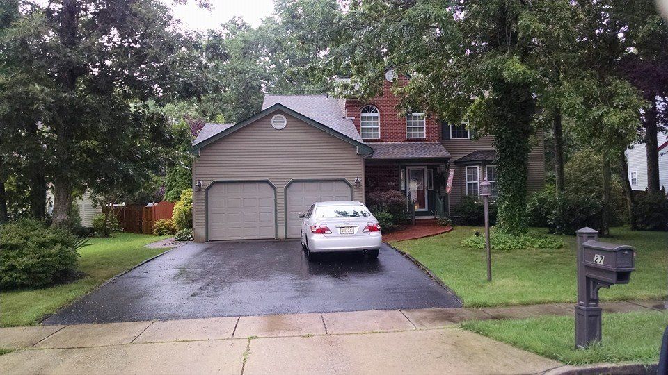 A two-story house with a two-car garage. A white car sits in the driveway, which is wet.