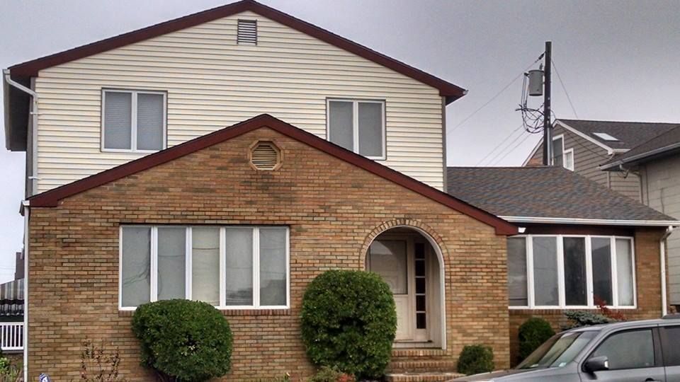 Two-story house with brick facade, beige siding, and white-framed windows; shrubbery in front.