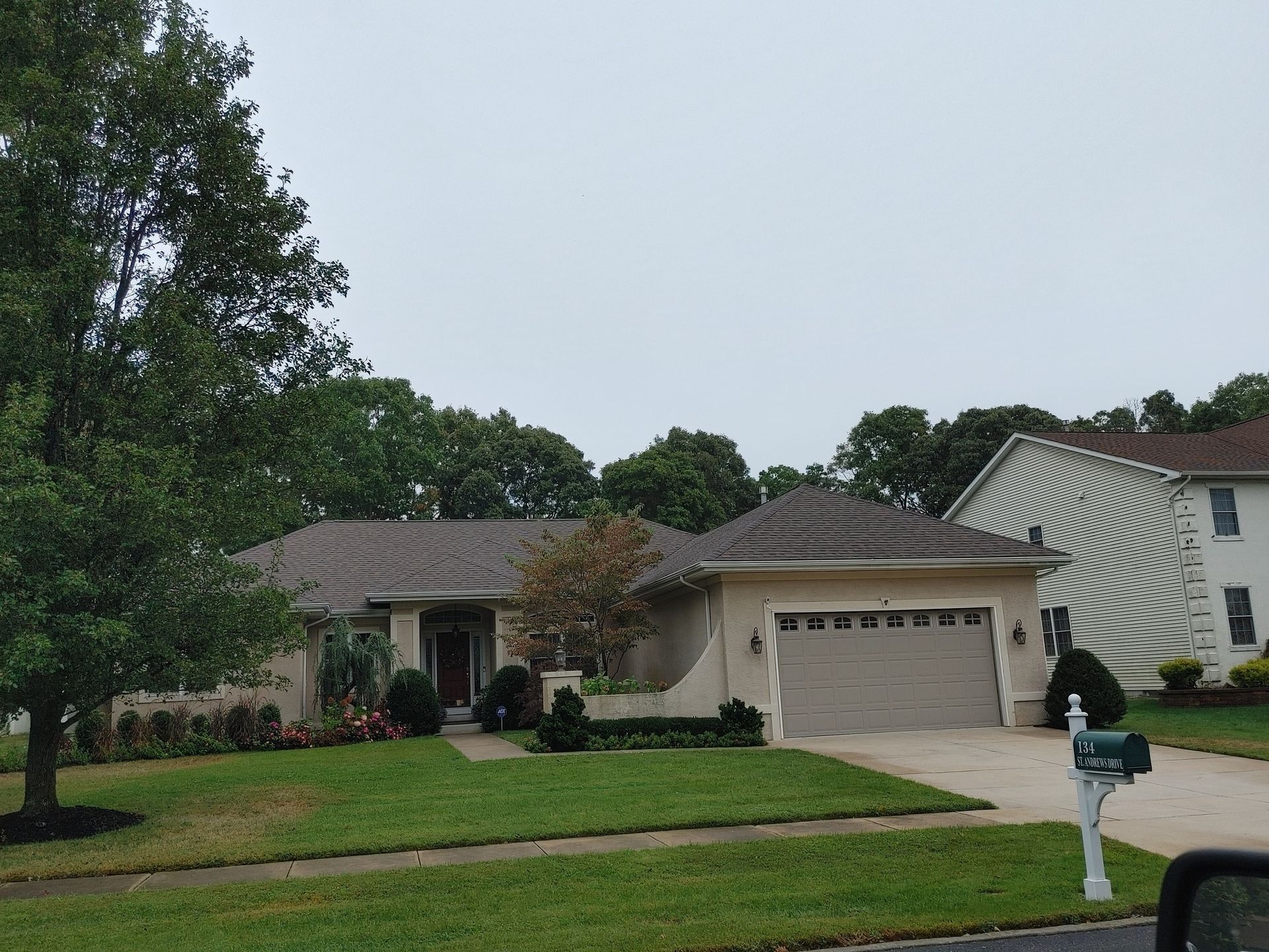 A beige, one-story house with a garage and green lawn, under a cloudy sky.