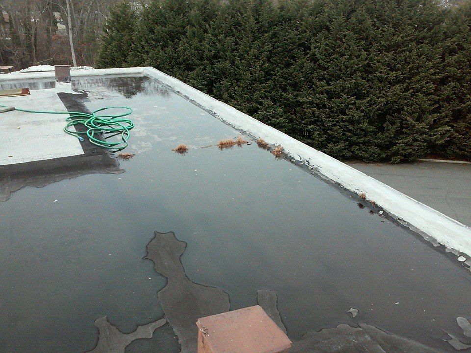 Flat rooftop covered in standing water, hose, and debris.