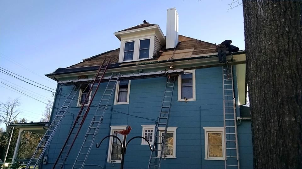 Blue house with ladders propped against it, roof being worked on. Person near chimney.