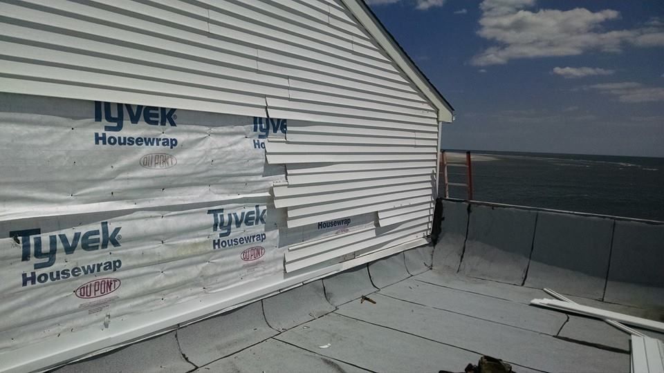 White siding installation with Tyvek house wrap, partially obscuring the flat roof and ocean view.