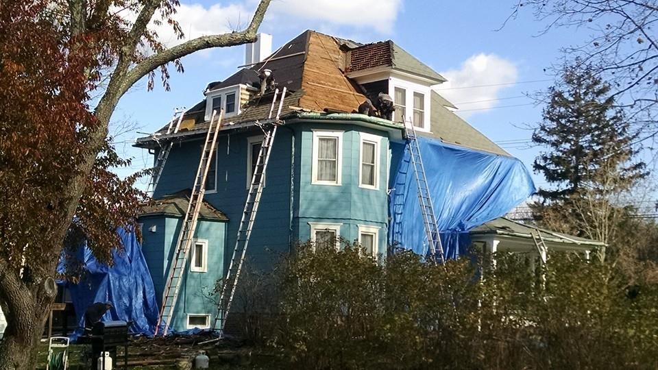 Blue house under construction with ladders and blue tarps on roof.