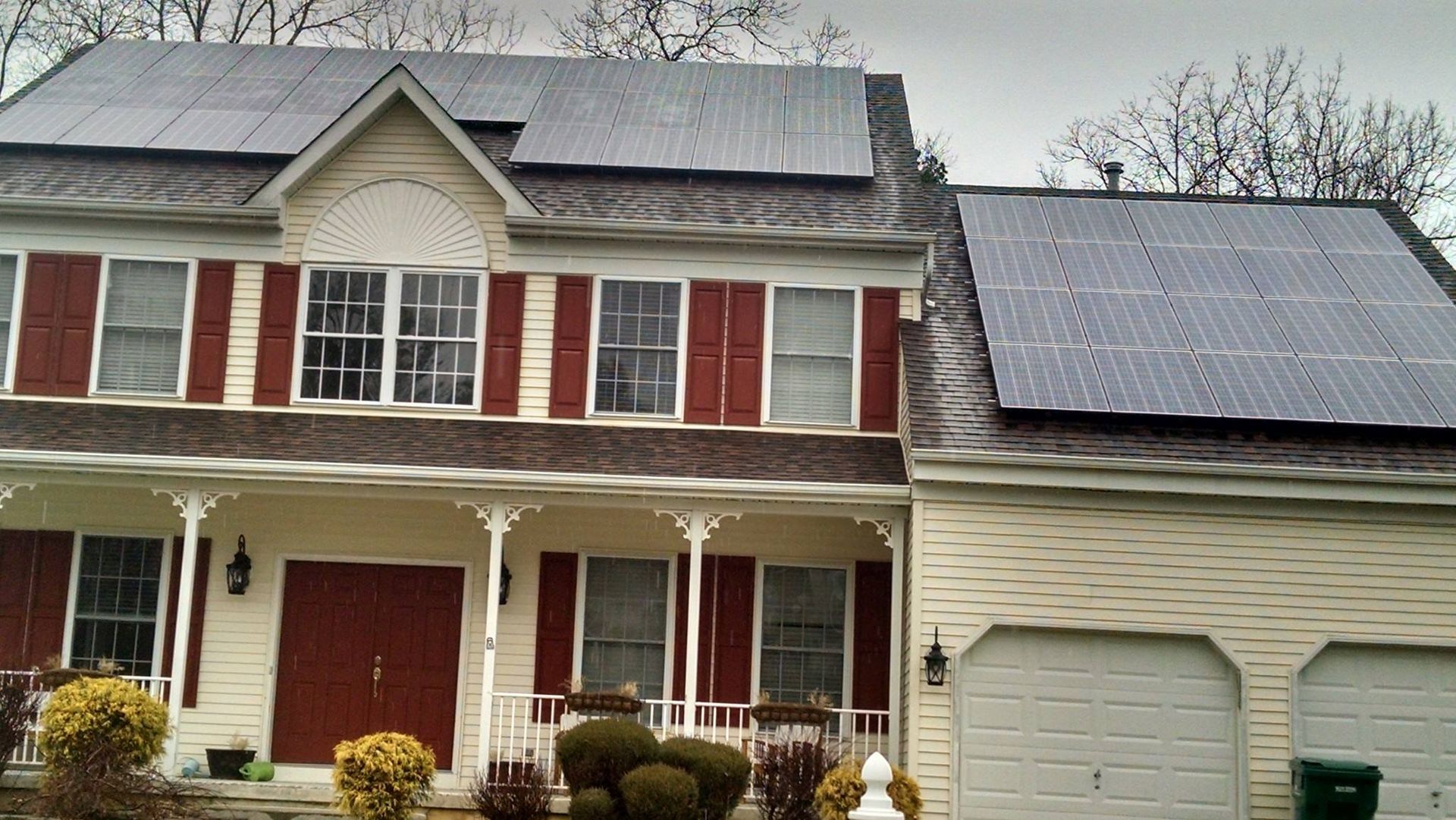 A two-story house with solar panels on the roof. Red shutters accent the windows.