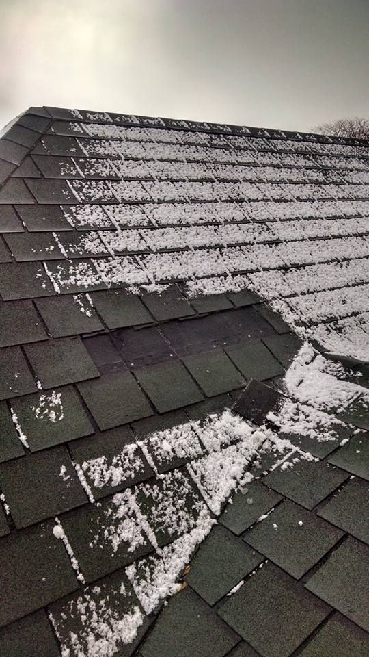 Snow-covered rooftop with dark asphalt shingles, sunlight, and a cloudy sky.