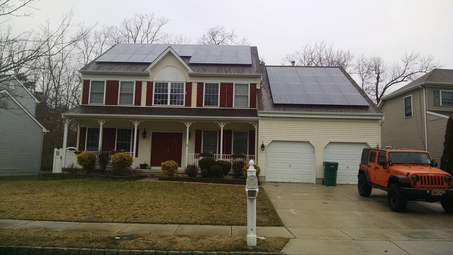 Two-story house with solar panels on the roof, attached garage, and orange Jeep parked in the driveway.
