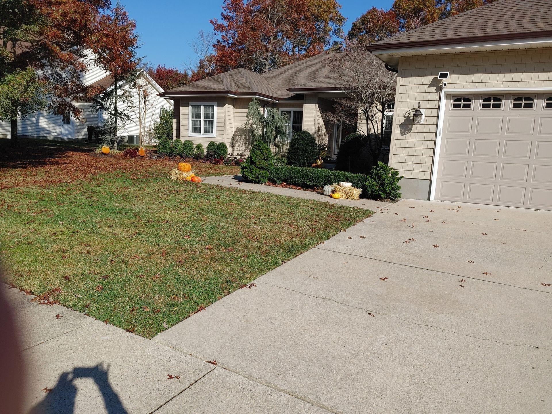 House exterior with lawn, driveway, fall foliage, and pumpkins. Beige garage, brick facade.