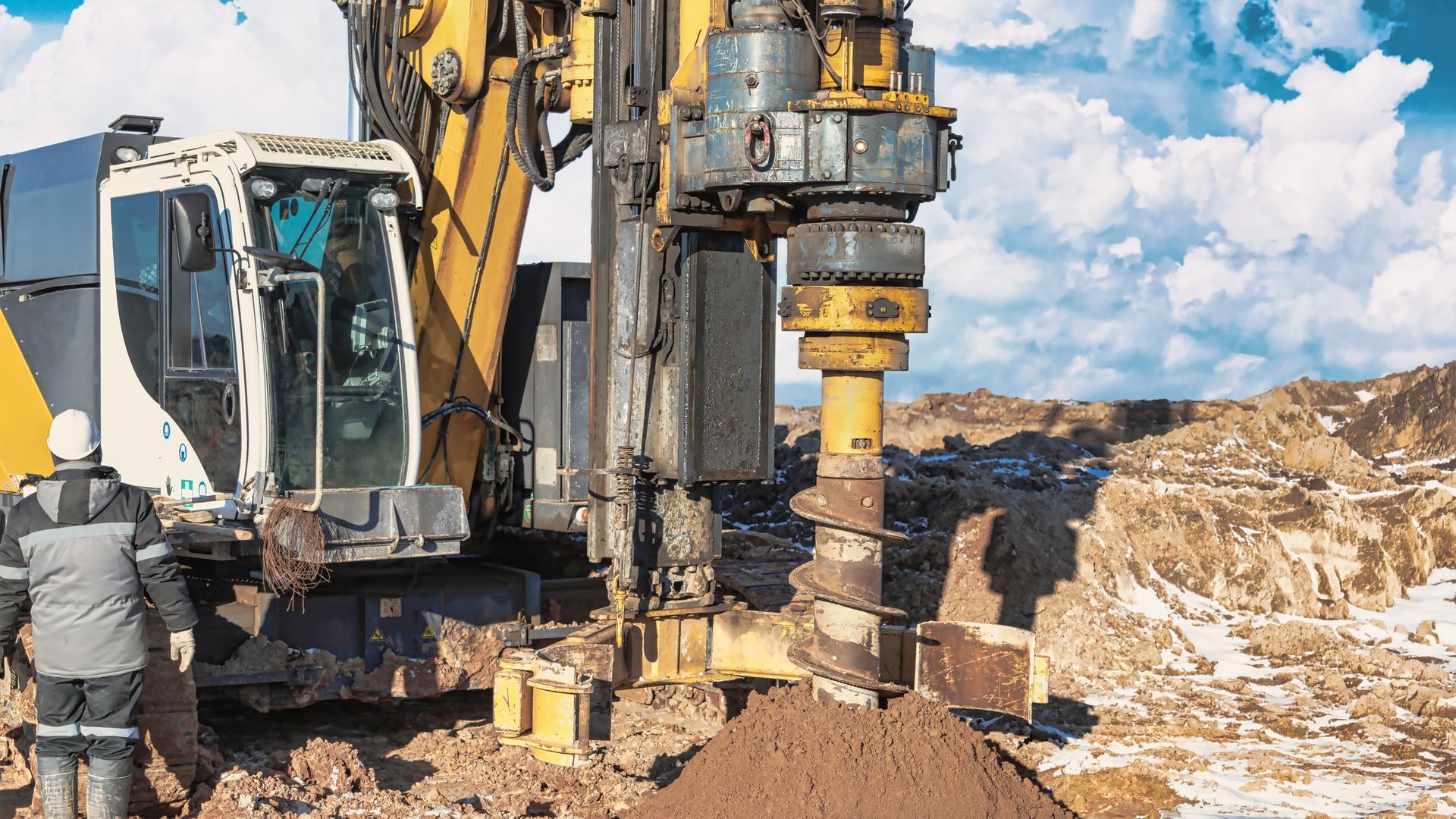 Construction workers operating a drilling rig on a rocky site under a blue sky