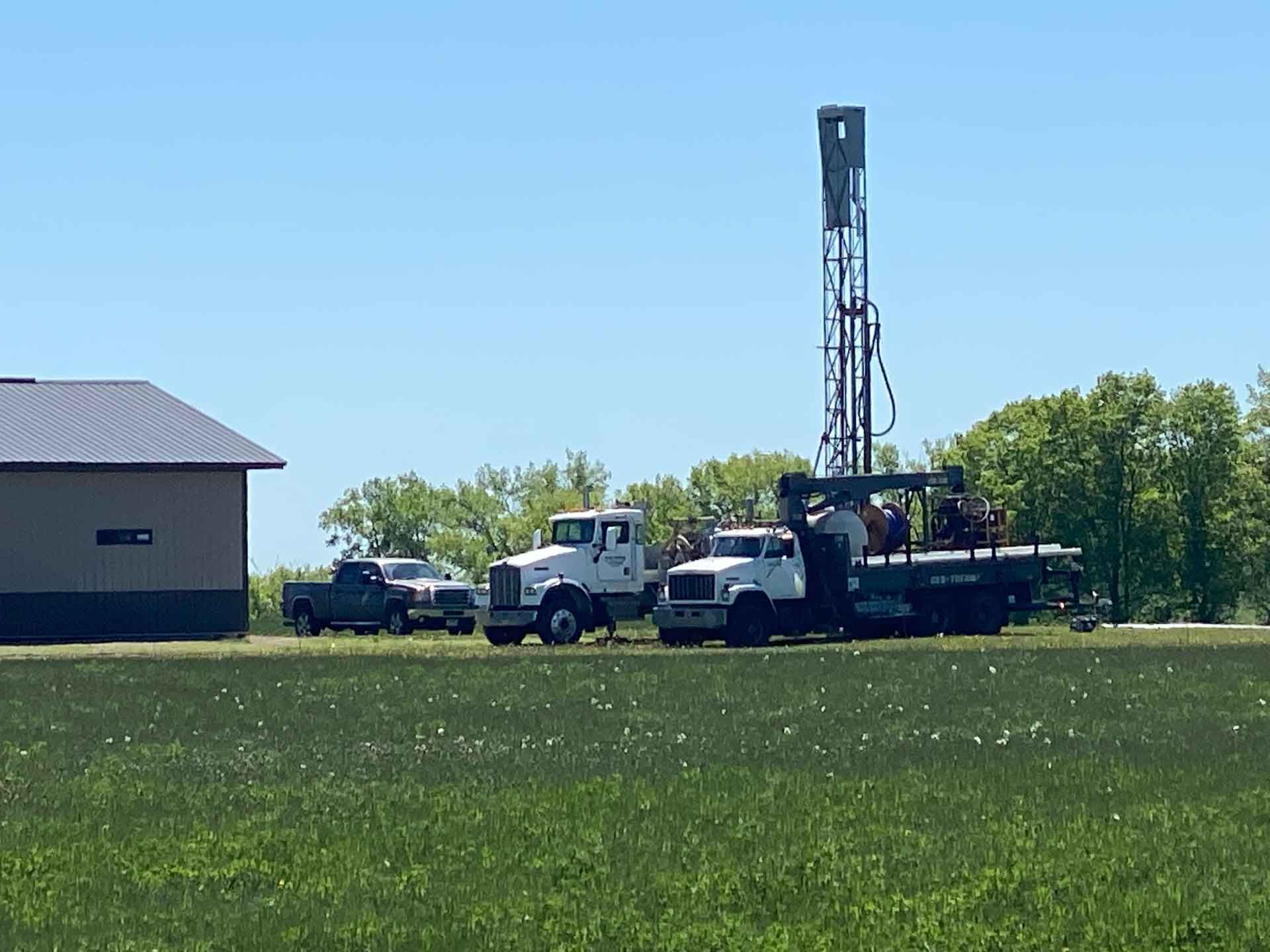 A group of trucks are parked in a grassy field next to a building.