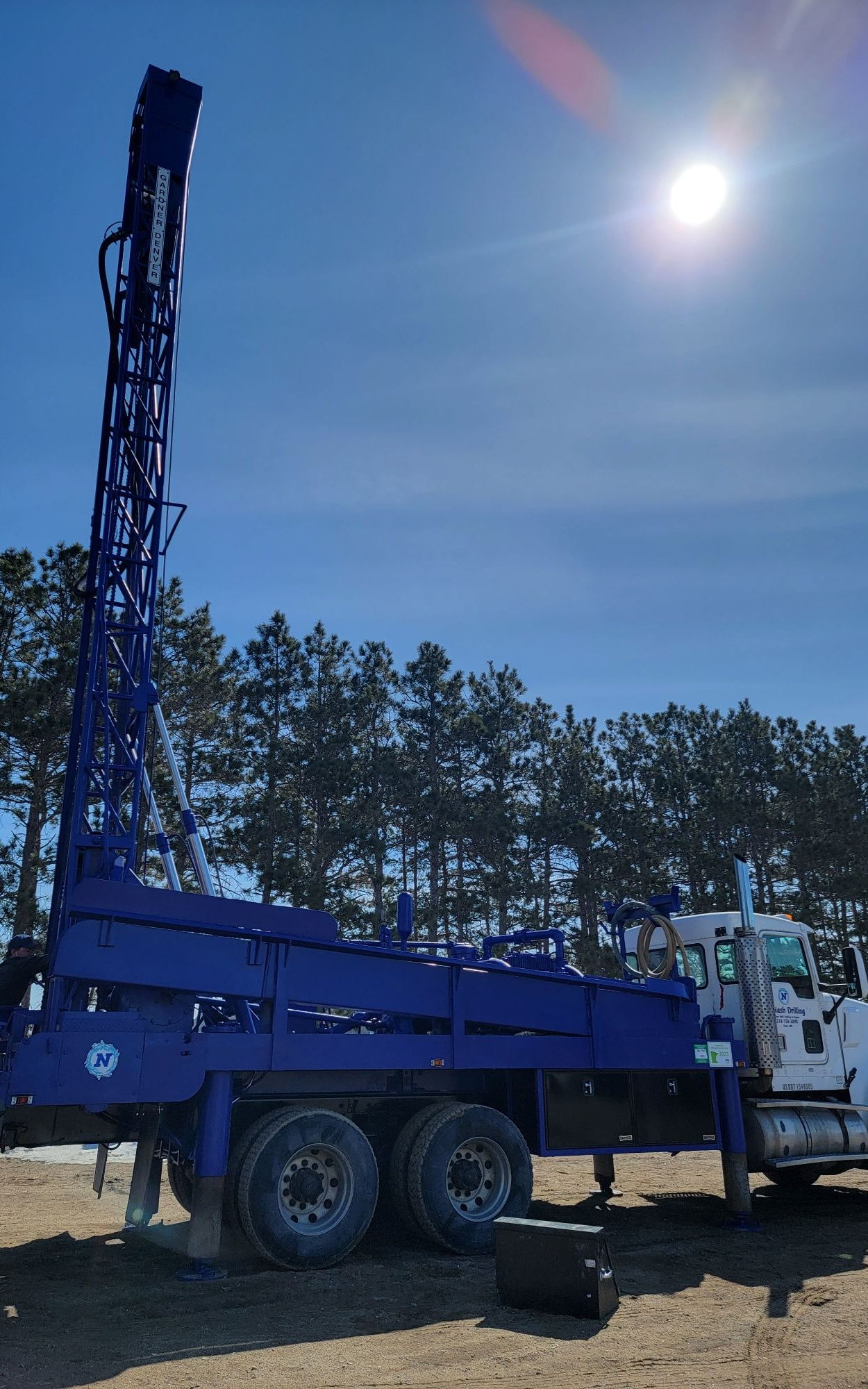Blue drilling rig on a truck, outdoors with a sunny sky and trees.