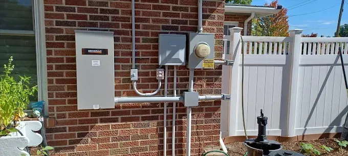 Electrical equipment mounted on a brick wall next to a white fence.