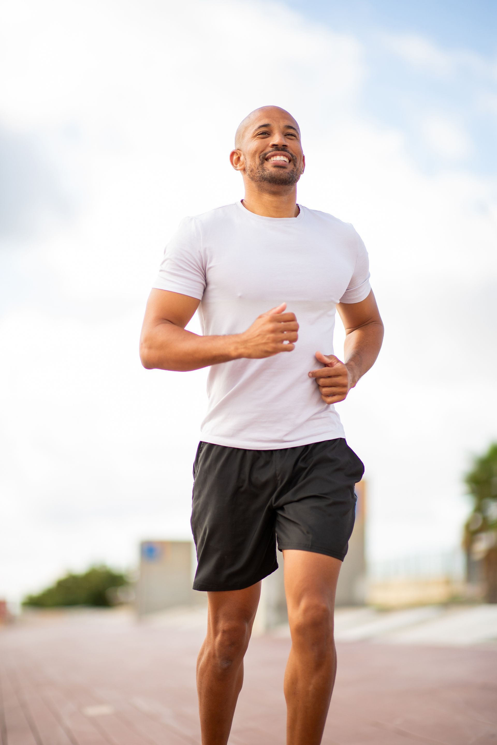 Man jogging outdoors on a paved path, wearing a white shirt and black shorts under a bright sky