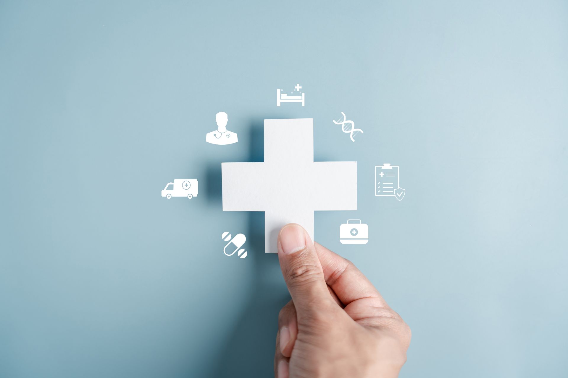 Hand placing a white medical cross icon on a light blue background with healthcare symbols