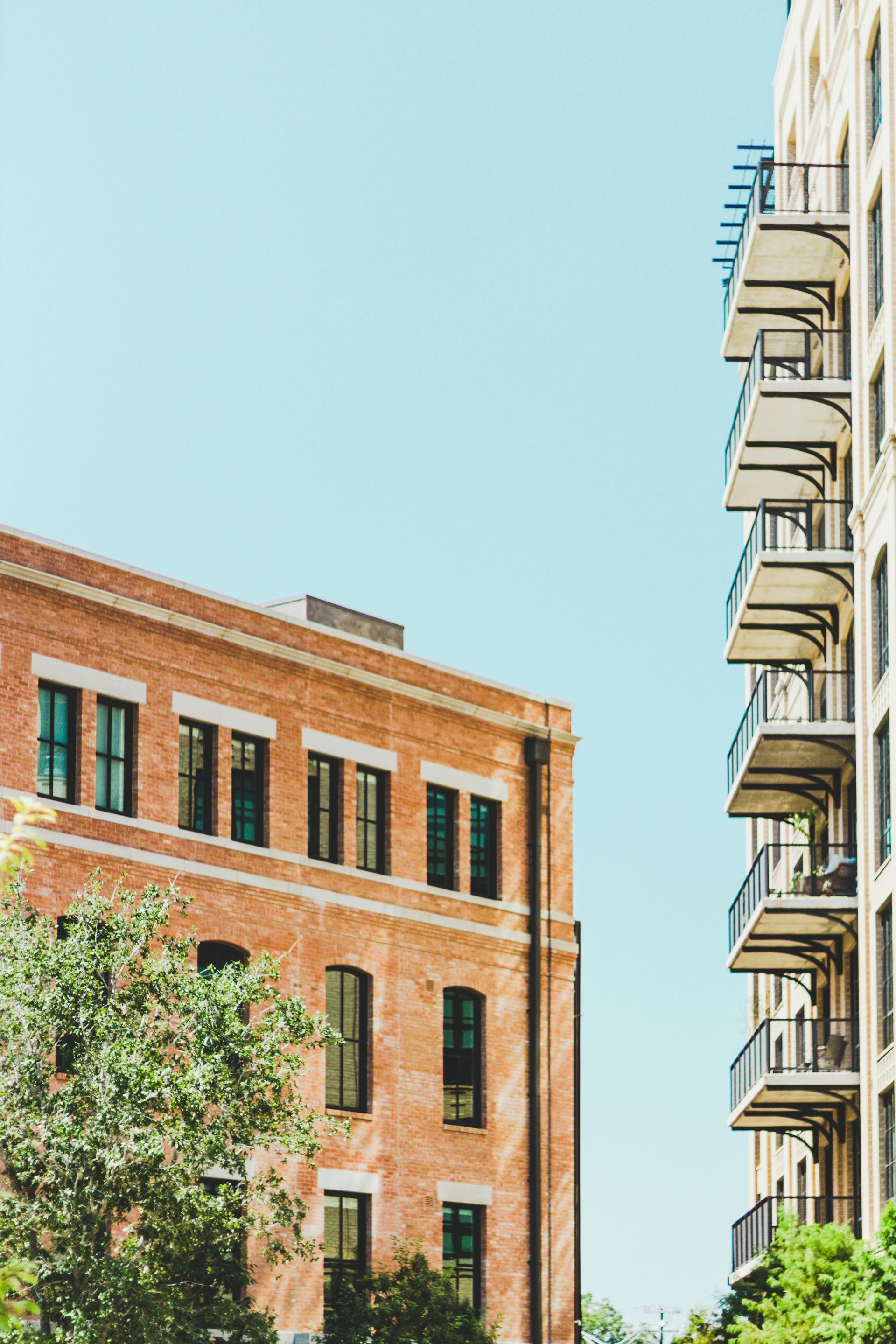 Red brick building beside a taller beige apartment building under a clear blue sky