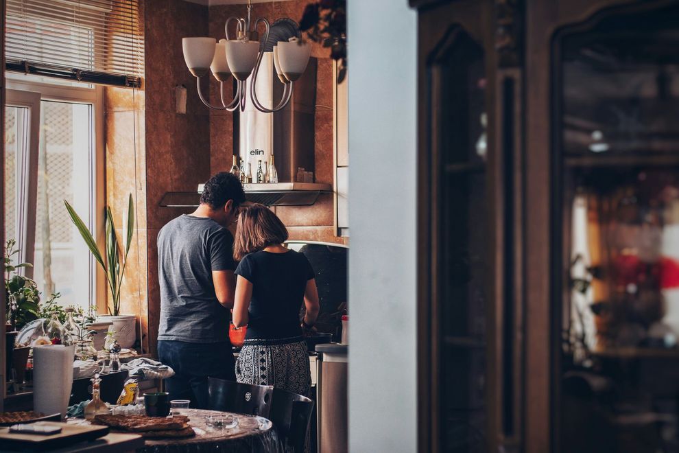 Two people standing at a rustic kitchen counter with plants and hanging lights in warm light