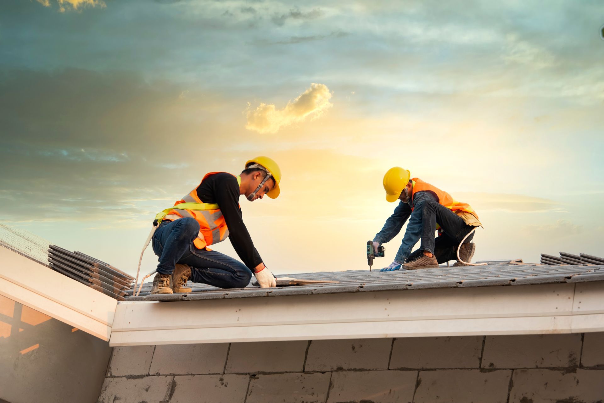 Construction workers installing roofing panels on a house roof, wearing safety gear at sunset. Construction workers installing roofing panels on a house roof, wearing safety gear at sunset.
