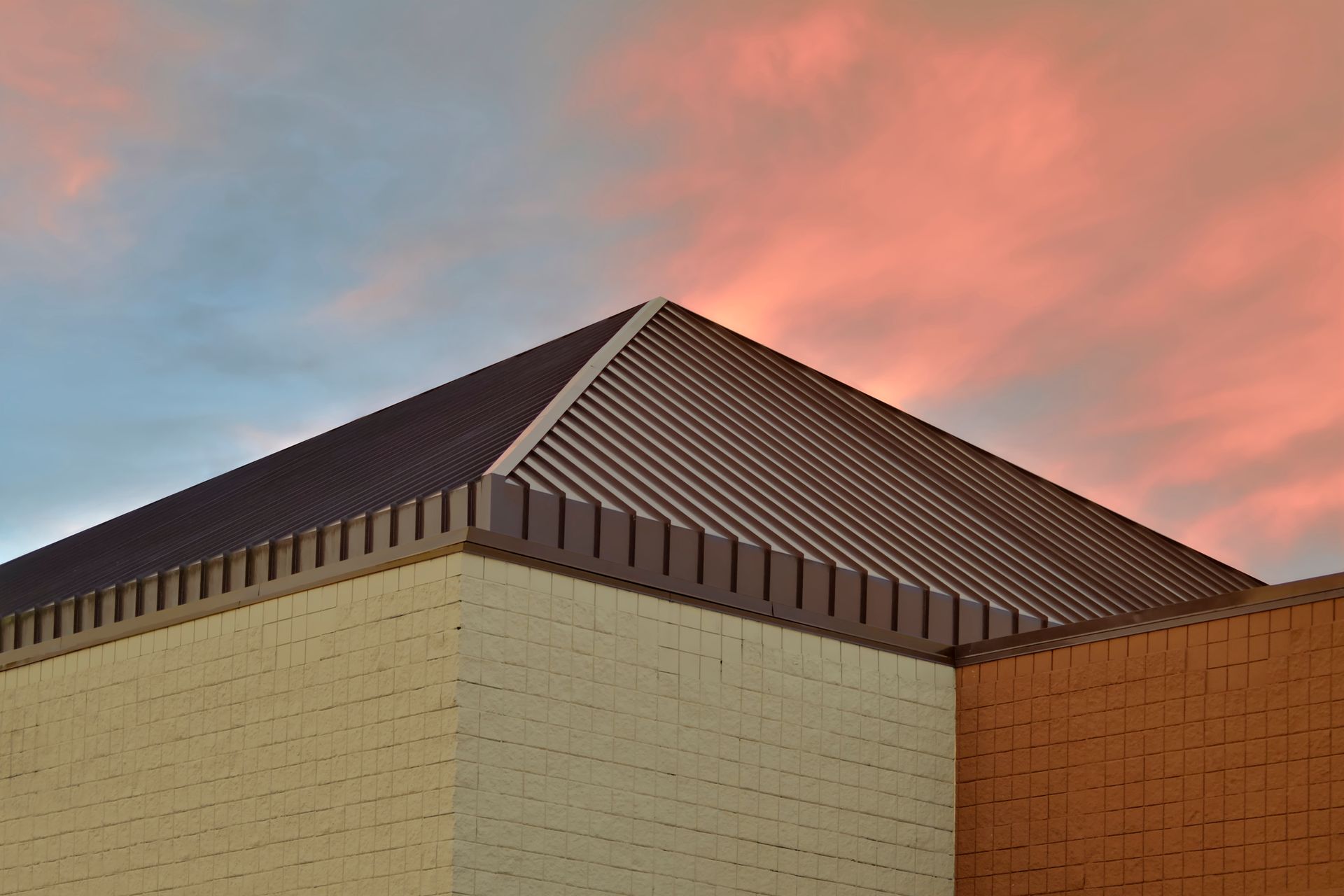 View of a corner of a commercial building’s roof with a sunset behind it.