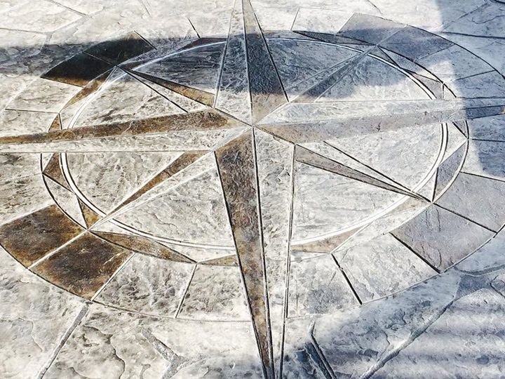 Stone compass rose mosaic on a paved surface, with gray, white, and tan geometric star segments.