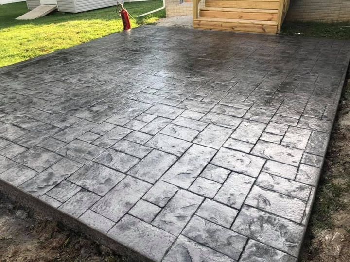 Freshly stamped gray concrete patio beside a lawn and wooden deck steps