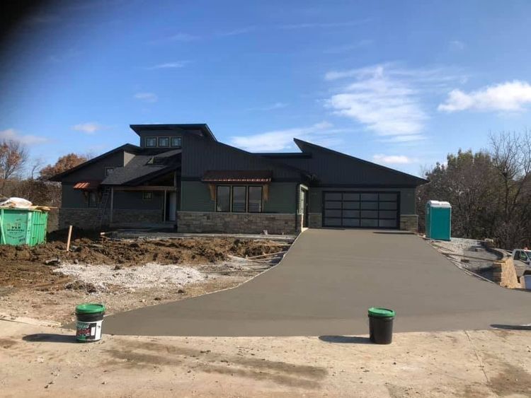 Modern dark house with a fresh concrete driveway under construction on a clear day